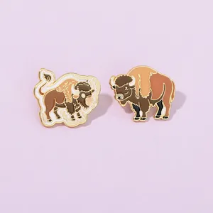 Detailed view of two bison enamel pins with gold trim on light purple background