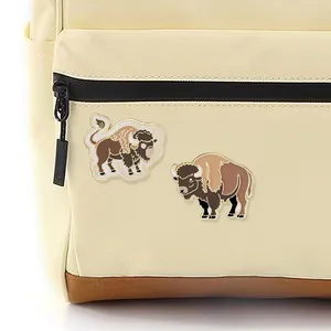 Set of two creative enamel yak pins displayed on a beige canvas backpack strap