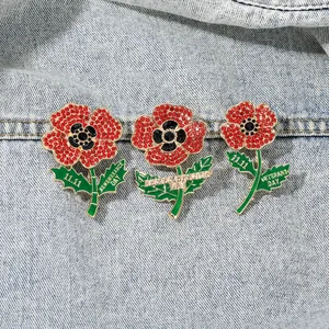 Detailed close-up of poppy flower brooches with red crystals on blue denim background