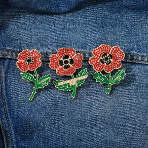 Detailed macro view of three red poppy brooches with crystal rhinestones and green enamel leaves