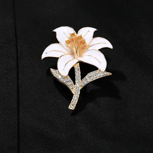 Detailed close-up of white enamel lily brooch with gold trim and sparkling rhinestones