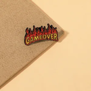 Pin esmaltado de dibujo animado con llamas rojas y texto Gameover en letras amarillas