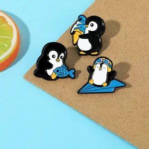 Dettaglio di tre spille in smalto a forma di pinguino con motivi di gelato e aeroplano
