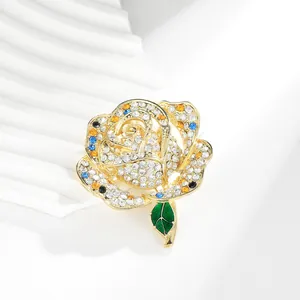 Macro detail of rose brooch with white rhinestones and green enamel leaf on gold metal