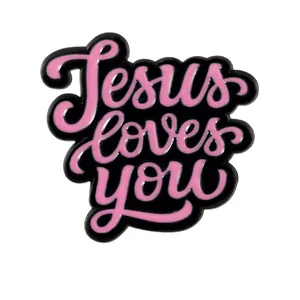 Close-up of pink 'Jesus loves you' script on a black enamel pin with silver metal edges