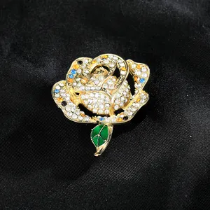 Elegant rose brooch with white rhinestones and green enamel leaf on black texture