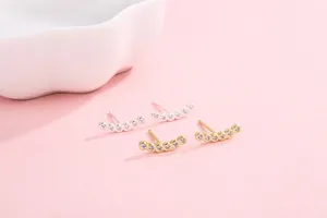 Macro view of gold and silver S925 silver ear crawlers with zircon stones on pink background