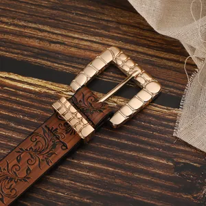 Close-up of brown leather belt with embossed floral pattern and gold rectangle buckle