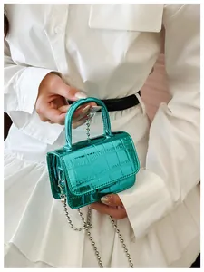 Detail of mini green crocodile pattern handbag with silver chain strap and top handle