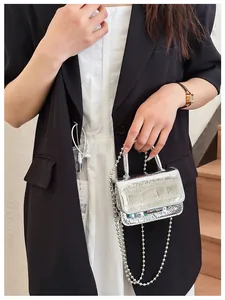 Detail of silver mini handbag with crocodile pattern and beaded chain held by model