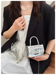 Detail of silver crocodile-embossed trapezoid handbag with sleek metal chain and top handle