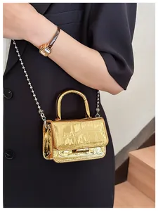 Detail of a mini gold crossbody bag featuring crocodile texture and a silver bead chain