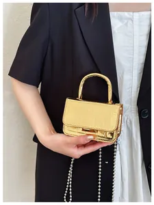 Detail of a golden crocodile texture mini handbag with a metallic finish and chain strap