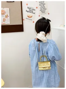 Detail of girls' golden metallic crossbody bag with textured crocodile pattern and chain