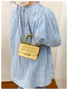 Close-up of golden mini crossbody bag with embossed crocodile pattern and ball chain