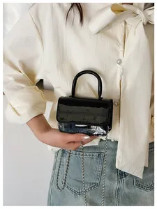 Detail of a black glossy crocodile pattern mini bag with a silver ball chain strap