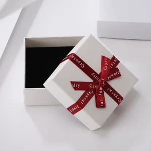 Elegant off-white textured jewelry gift box with black velvet interior and red ribbon bow