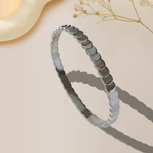 Silver stainless steel bangle with a unique geometric fish scale pattern on warm background