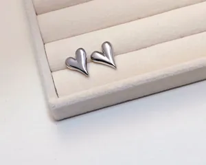 Macro shot of silver heart stud earrings with a high-polish finish on velvet display