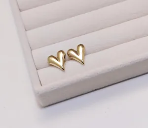 Macro shot of polished gold heart stud earrings on a cream velvet jewelry tray