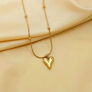 Detail of gold heart pendant necklace on silk featuring round beads and sleek snake chain
