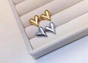 Close-up of gold and silver heart-shaped stud earrings in a beige velvet jewelry box