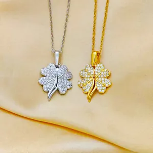 Goldene und silberne Kleeblatt-Halsketten mit weißen Zirkonia auf gelbem Seidenhintergrund