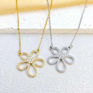 Close-up of gold and silver flower pendants with white cubic zirconia on a stone surface