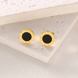 Minimalist gold and black roman numeral stud earrings on a textured stone base