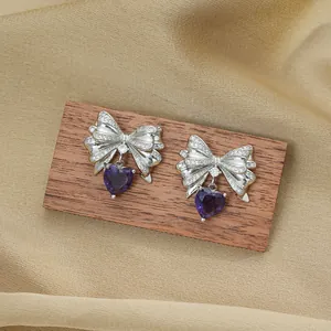 Titanium steel bowknot heart earrings with purple zircon on a warm satin background