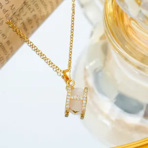 Gold H-letter necklace with opal stone and zircon accents on vintage background