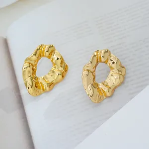 Détail macro de boucles d'oreilles dorées à texture lave et éclat métallique poli