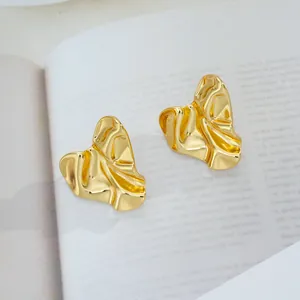 Détail de boucles d'oreilles dorées irrégulières avec texture plissée sur magazine