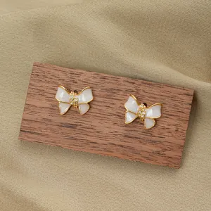 Detail of sweet bow-shaped earrings with cream pearl finish and sparkling zircon inlay