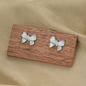 Detail of sweet bow-shaped earrings with milky white glaze and fine crystal inlay