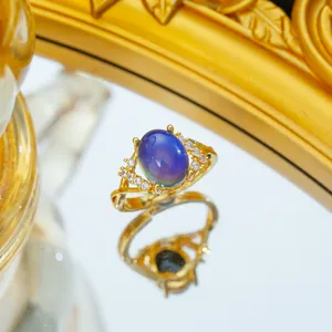 Goldener Kreuzring mit farbwechselndem Stein und kleinen Diamanten auf weißem Hintergrund