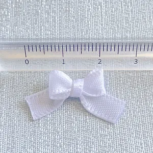 Detail shot of a 2.5cm white satin ribbon bow with ruler showing size for DIY crafts