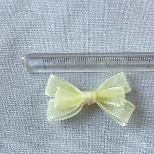 Detailed view of 4.5cm yellow organza bow with white stitching and scale ruler