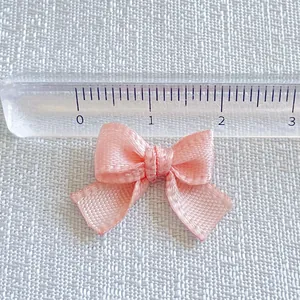 Macro shot of a 2cm pink satin ribbon bow accessory with ruler for size measurement