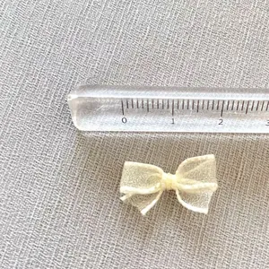 Close-up of a 1.5cm cream mesh bow accessory with a ruler showing its small size and texture