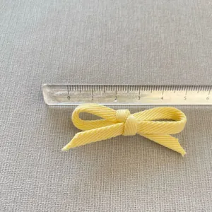 Detail view of a 6cm light yellow fabric bow accessory with a ruler measuring its size