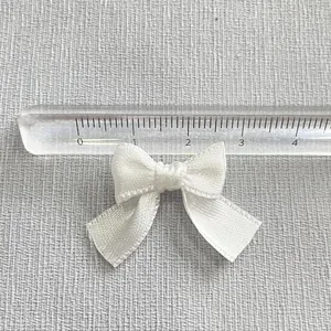 Close-up of a 3cm white satin ribbon bow accessory with ruler for size measurement