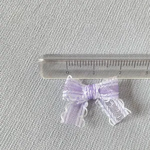 Gros plan d'un nœud en maille violette de 2,5cm avec dentelle blanche sur tissu gris