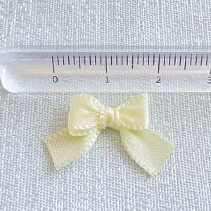 Macro shot of a small beige satin ribbon bow next to a ruler for precise size measurement