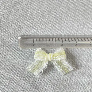 Détail d'un mini nœud en dentelle jaune rayé de 2,5 cm avec mesure par règle
