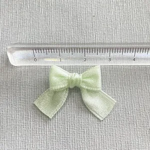 Close-up of small light green satin bow accessory with ruler showing 3cm width scale