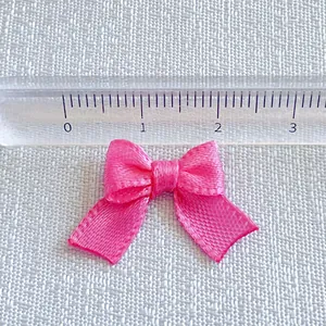 Detail view of pink satin ribbon bow with ruler showing 25mm size for DIY accessories