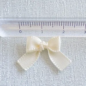 Macro view of a 2.5cm cream satin ribbon bow with ruler showing precise DIY craft dimensions