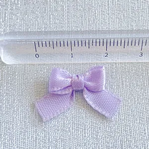 Detailed view of a 2.5cm light purple satin ribbon bow showing texture and size with a ruler
