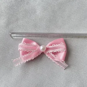 Dettaglio di un fiocco di raso rosa da 7,5cm con pizzo e una perla bianca centrale